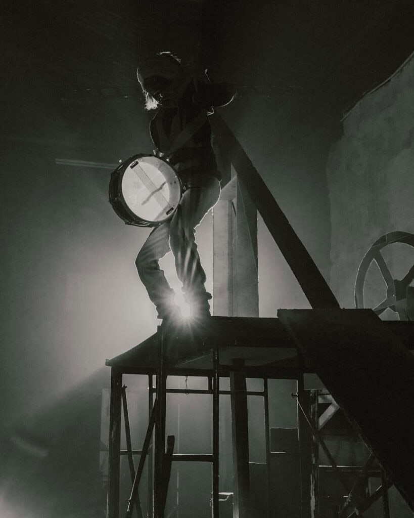 Backlit silhouette standing atop industrial scaffolding, capturing the cinematic tension present in themes surrounding KABEAUSHÉ’s creative world.