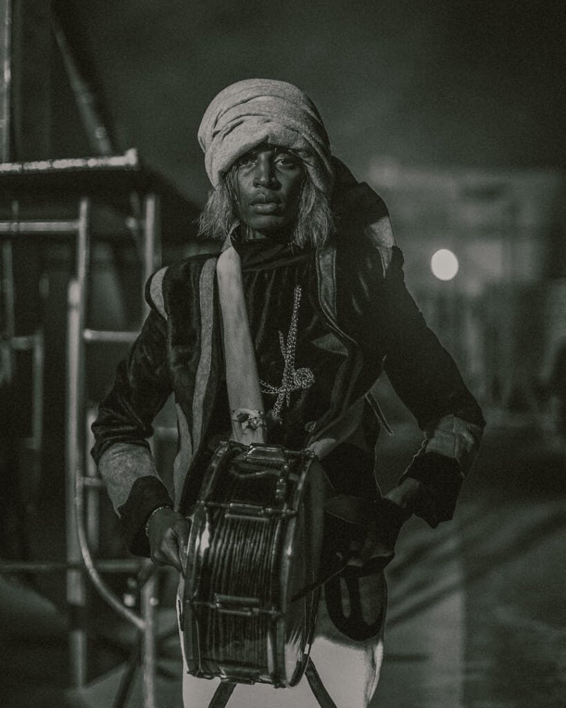 Moody monochrome portrait of a performer holding a drum, echoing the rhythmic intensity central to KABEAUSHÉ’s musical universe.