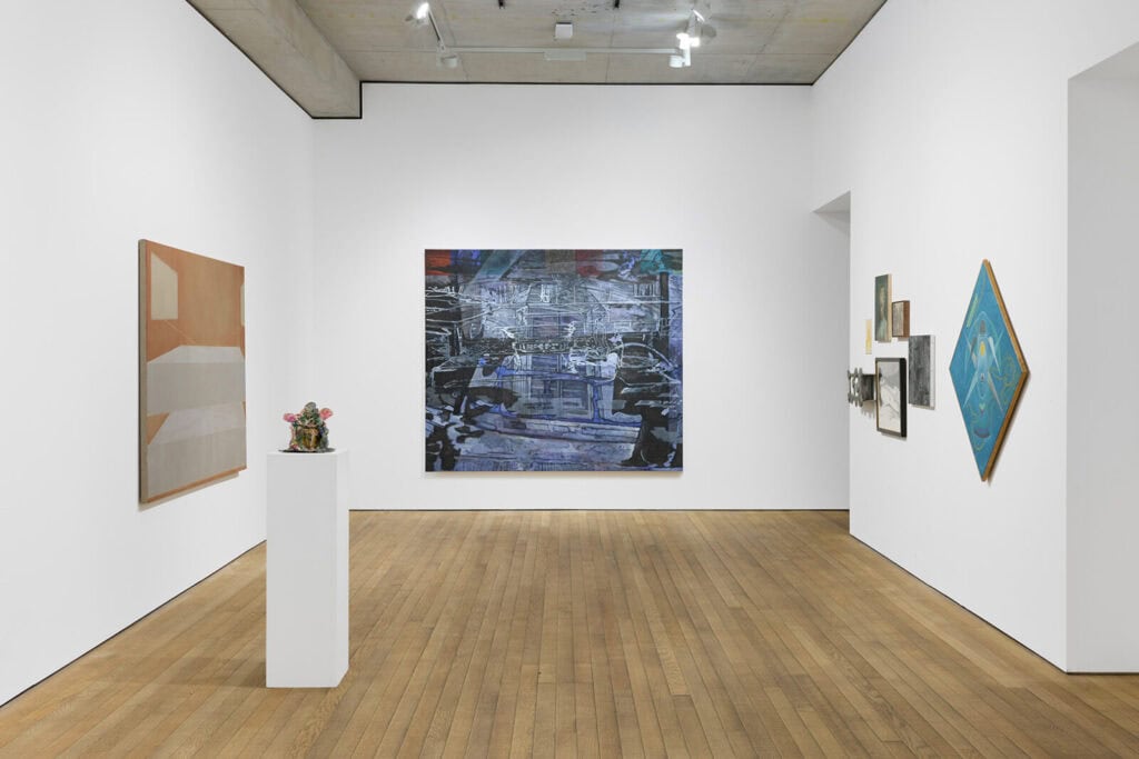 A contemporary art gallery features abstract paintings on white walls, a sculpture of small colorful objects on a pedestal, and wooden flooring under bright lighting as part of Crude Hints Towards curated by Charlotte Edey at Ginny on Frederick for Frieze 2025.