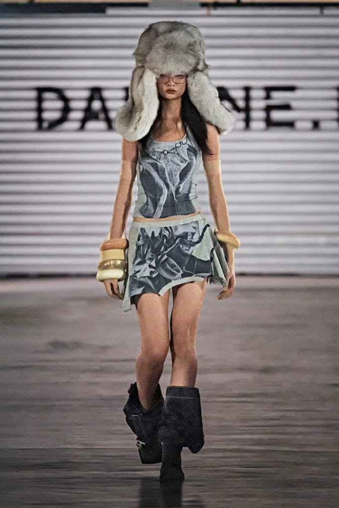 Model in printed mini dress and oversized fur hat from Daphne.lab × Marrknull’s gender-fluid “In a Hurry” runway show.