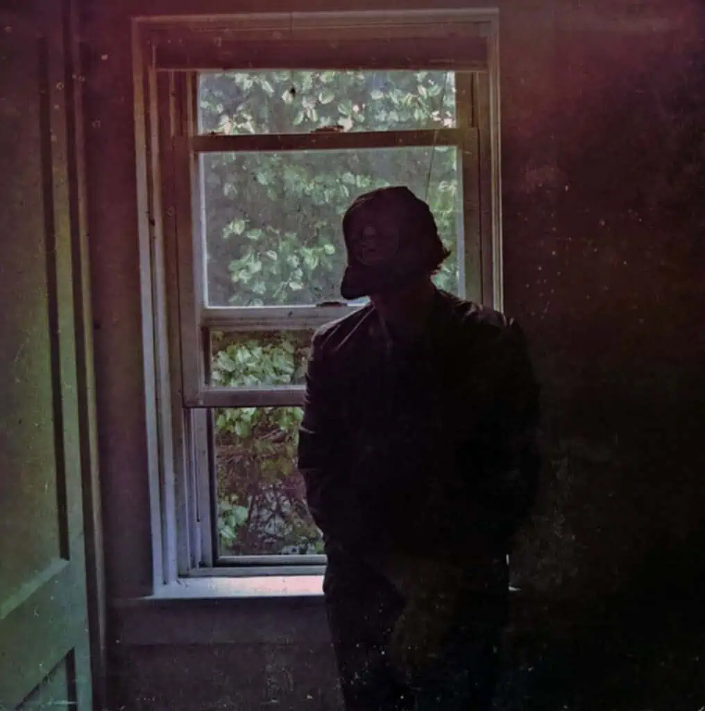 Public Memory artist near studio speakers by a bright window, captured in a moody, atmospheric, trip-hop style.