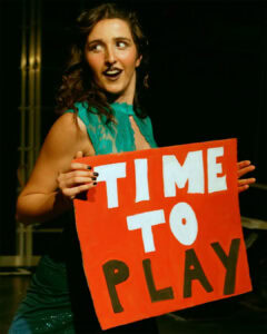 Sofia Natoli performing Babel Beast, holding a red “Time to Play” sign on stage.