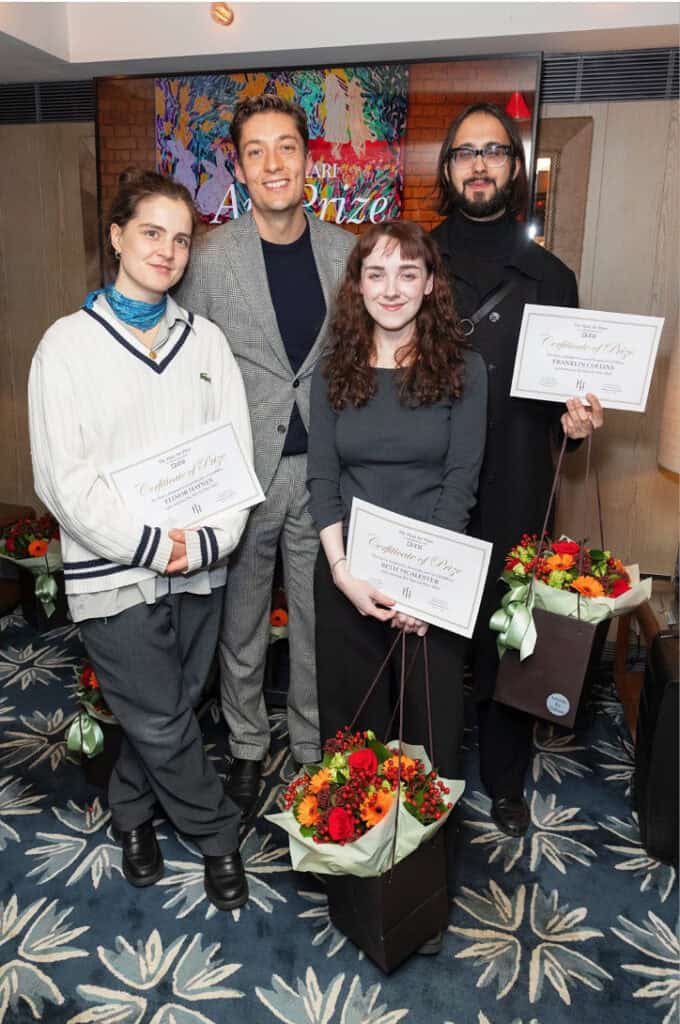 Four people pose indoors, three holding certificates and flower bouquets. Two women stand in front, with a man in a checked suit and another in glasses behind them. A colorful painting hints at The Hari Art Prize celebrating London’s emerging artists.