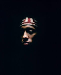 A person wearing a patterned knit headband is partially illuminated against a dark background, with most of their face and surroundings in shadow.