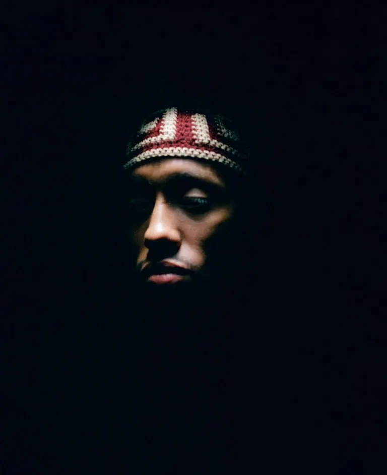 A person wearing a patterned knit headband is partially illuminated against a dark background, with most of their face and surroundings in shadow.