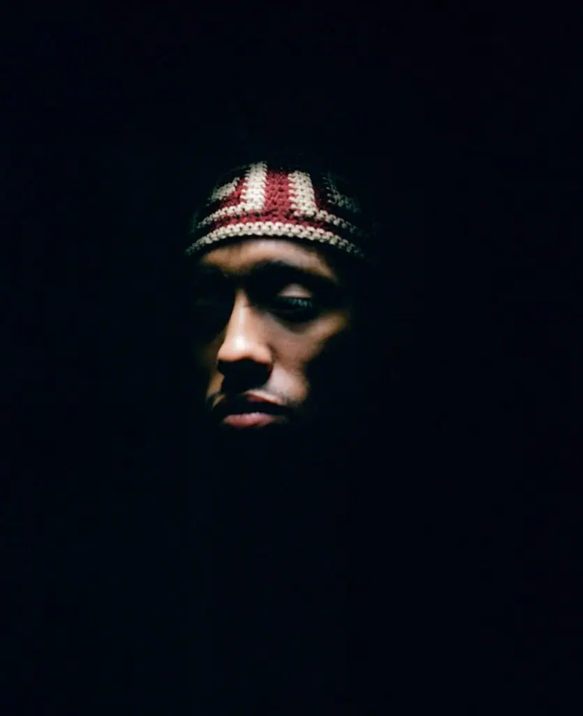 A person wearing a patterned knit headband is partially illuminated against a dark background, with most of their face and surroundings in shadow.