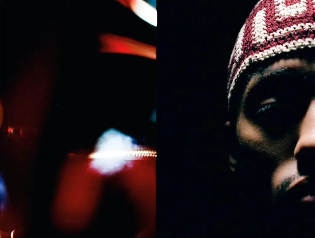 A dimly lit close-up photo shows the right side of a persons face wearing a patterned knit cap. The left half of the image is blurred with red, dark, and white light streaks.