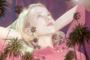 A blonde woman in a pink top reclines with her hands behind her head, gazing upward dreamily. Semi-transparent palm trees overlay the image, giving it a surreal effect reminiscent of a still from Mulholland Drive.