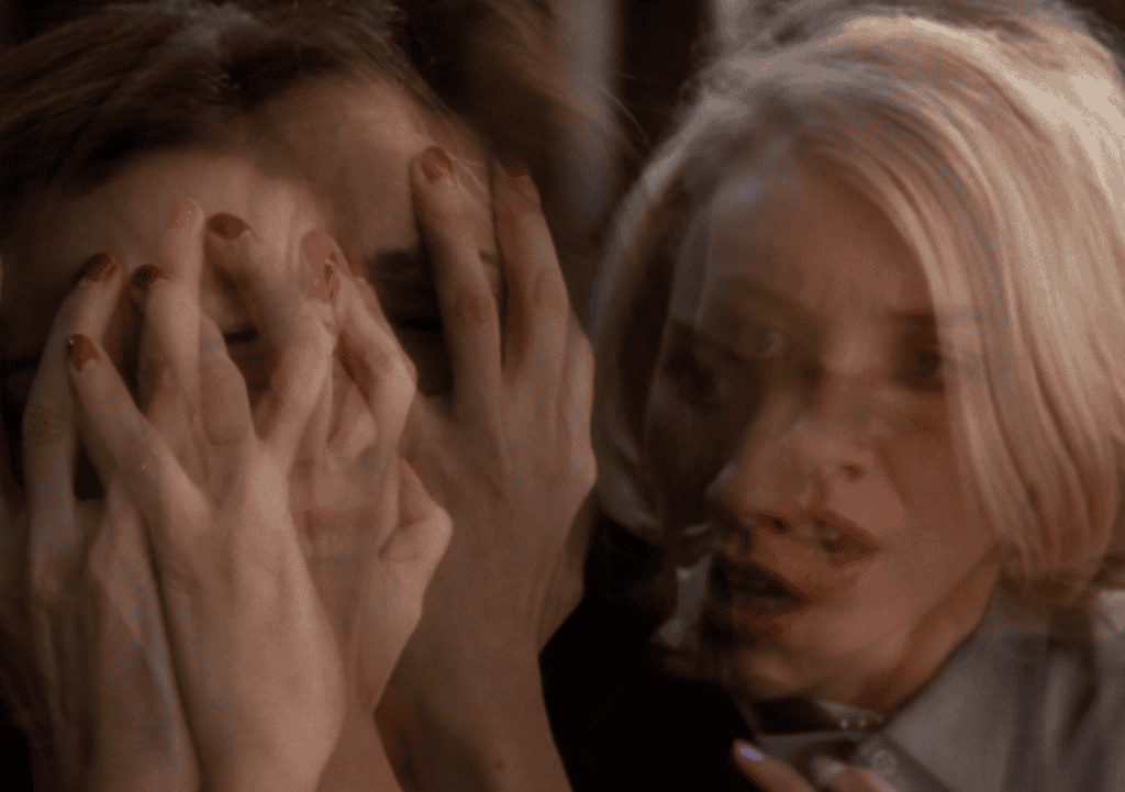 A blurred, double-exposed image of two women: one covering her face with her hands, and the other with an anxious expression, both with visible red nail polish.