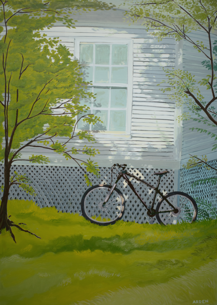 A bicycle leans against the white lattice foundation of a house with light siding and a large window. Green grass and leafy trees frame the foreground, casting dappled shadows in the scene.