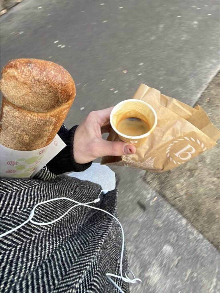 A person holding a cup of coffee and a bagel.