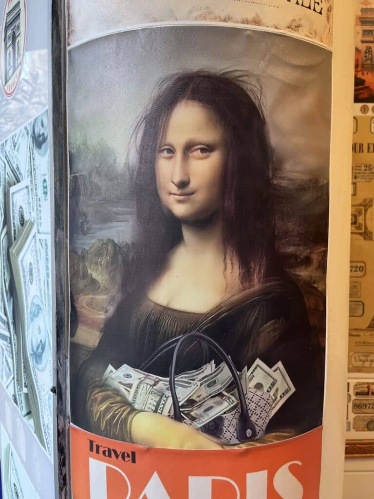 A poster of the Mona Lisa holding a handbag filled with US dollar bills, with the text Travel PARIS at the bottom. The image is displayed next to dollar bill decorations on a wall.
