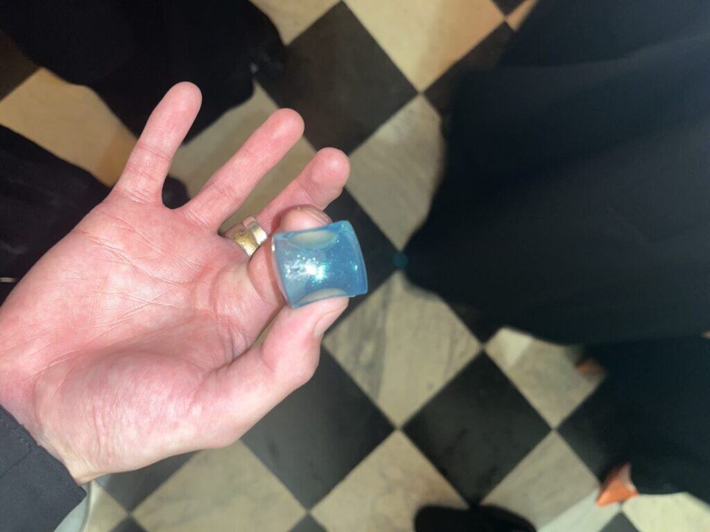 A hand holding a blue and white laundry detergent pod over a black and white checkered tile floor.