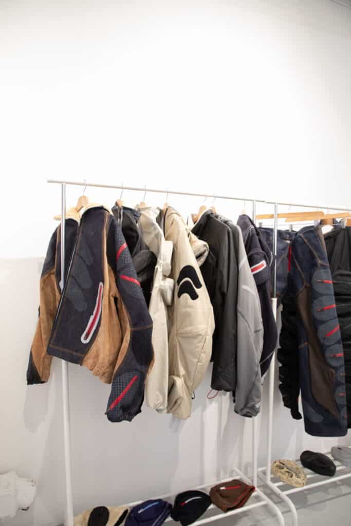A clothing rack displays several stylish jackets in various colors and designs, including brown, beige, gray, and dark blue, with unique patterns and details, against a white wall in a modern store setting.