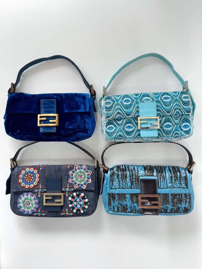 Four small designer handbags are arranged in a grid on a white background. Each bag has a unique blue-toned pattern and decorative buckle, with different textures, embroidery, and embellishments.