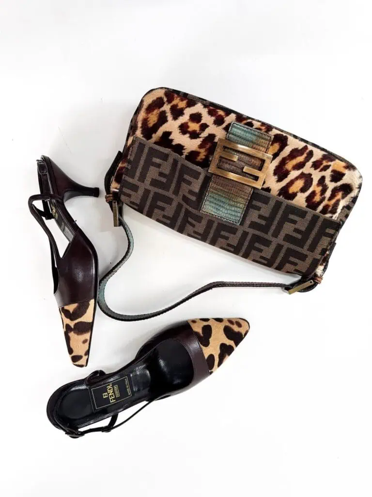 A pair of black and brown pointed-toe heels with leopard print accents next to a Fendi shoulder bag featuring brown monogram and leopard print patterns, all on a white background.