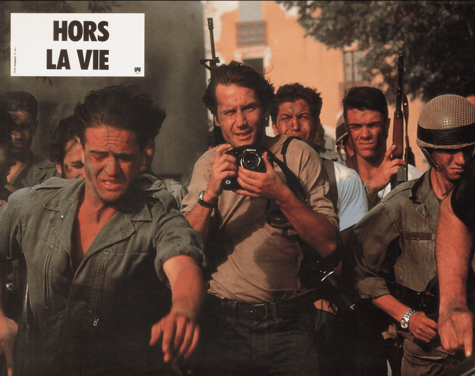 A group of tense men, including a photographer with a camera, are being led by armed soldiers. The scene is chaotic and intense. The top left corner displays the text hors la vie in bold letters.
