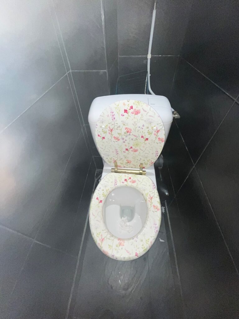 A toilet with a floral-patterned seat and lid, set against dark tiled walls in a small bathroom.