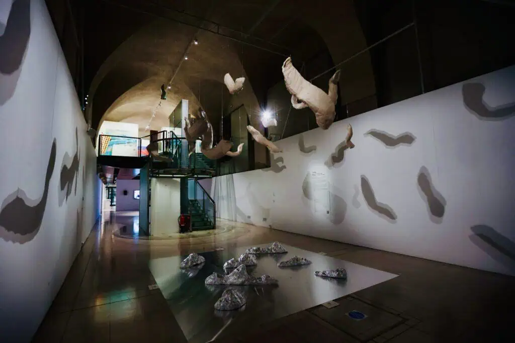 Interior view of a large-scale exhibition by Halise Karakaya, showing suspended sculptures and their dramatic shadows cast on gallery walls.