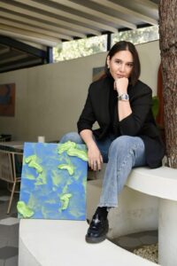 Artist Halise Karakaya posing with a textured blue and green abstract painting, showcasing her signature thick impasto technique.