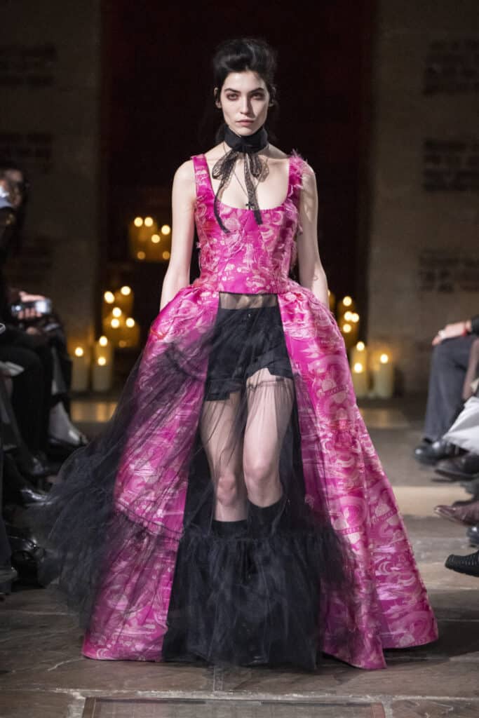 Model on the runway wearing a vibrant pink patterned corset top and a matching open-front skirt over black tulle layers by John Richmond