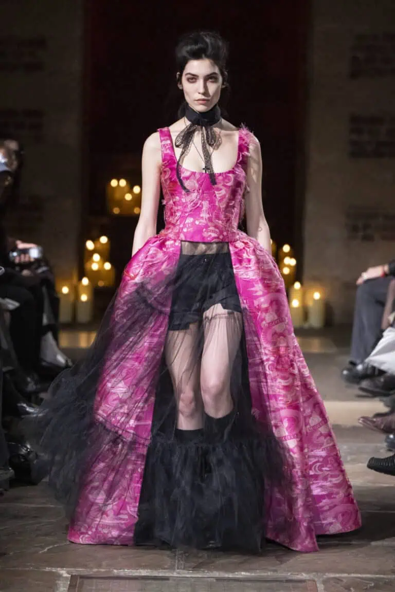 Model on the runway wearing a vibrant pink patterned corset top and a matching open-front skirt over black tulle layers by John Richmond