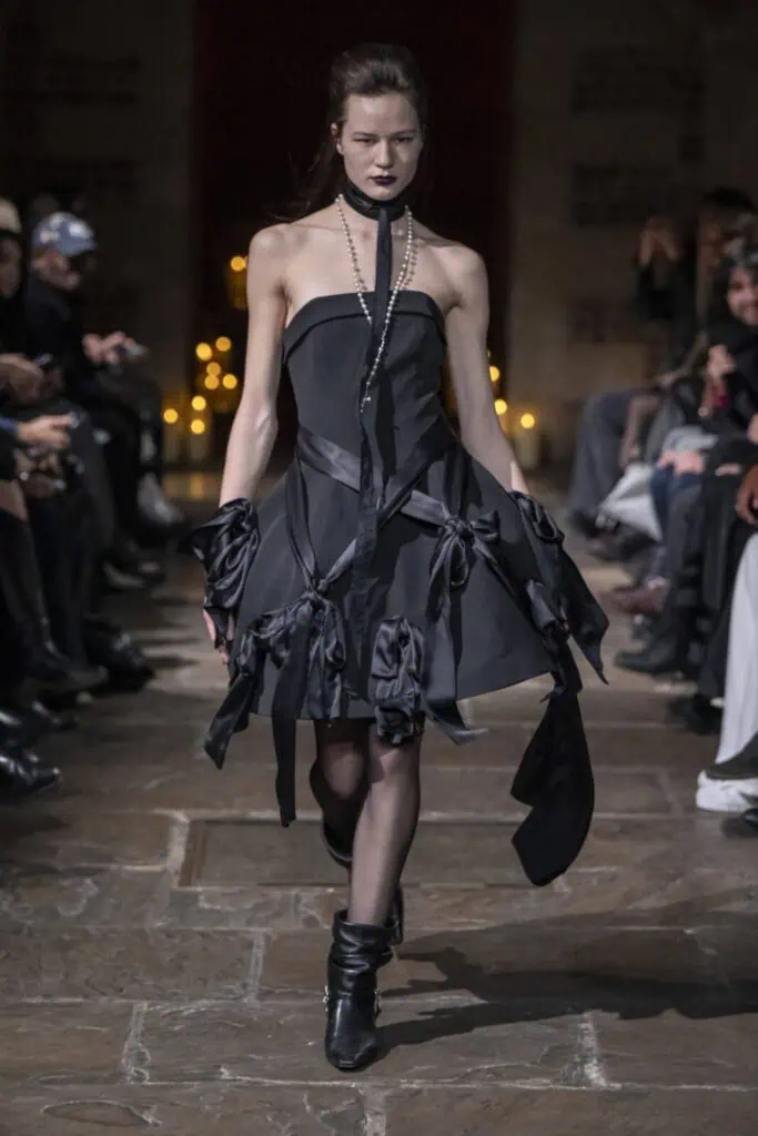 Model walking the runway in a black strapless mini dress with bow details for John Richmond