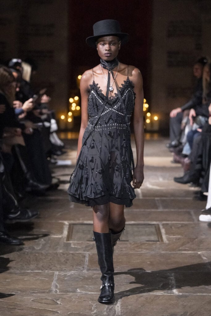 Model walking the catwalk in a black embellished slip dress and a top hat for John Richmond