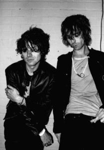 A grainy black and white portrait of The Hellp members posing against a white brick wall, showcasing their signature indie-sleaze and electronic punk aesthetic.