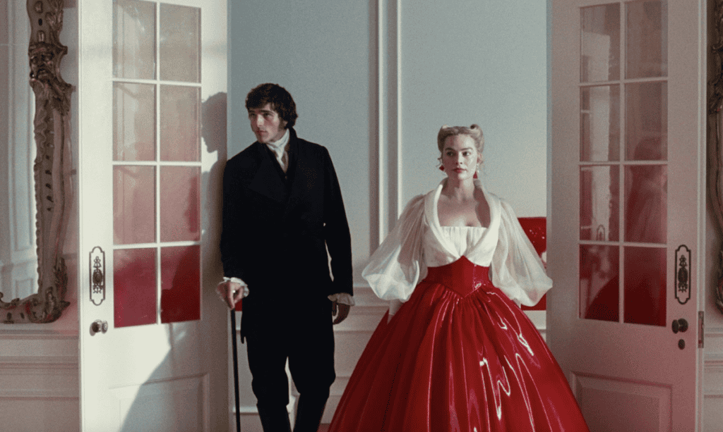 A man in a black suit and a woman in a dramatic red ball gown with sheer white sleeves stand side by side in an ornate room, framed by open white doors—a still from "Wuthering Heights" movie.
