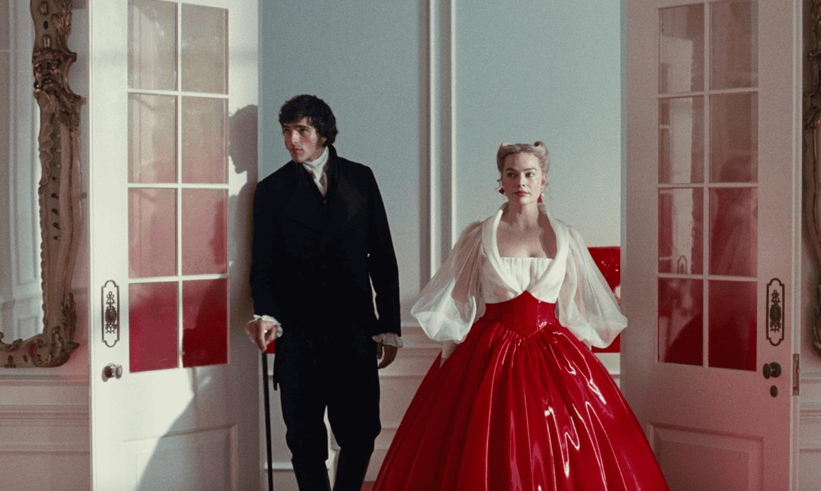 A man in a black suit and a woman in a dramatic red ball gown with sheer white sleeves stand side by side in an ornate room, framed by open white doors—a still from "Wuthering Heights" movie.