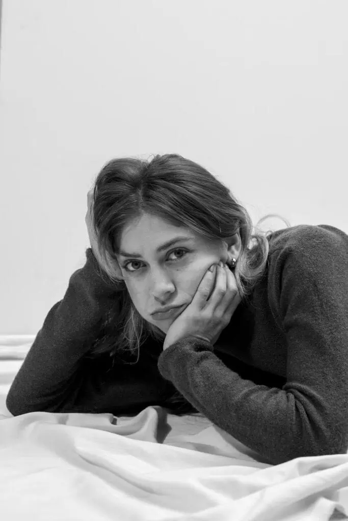 A black and white portrait of Madeline Cash, author of Lost Lambs, lying down and resting her head on her hand with a pensive expression.