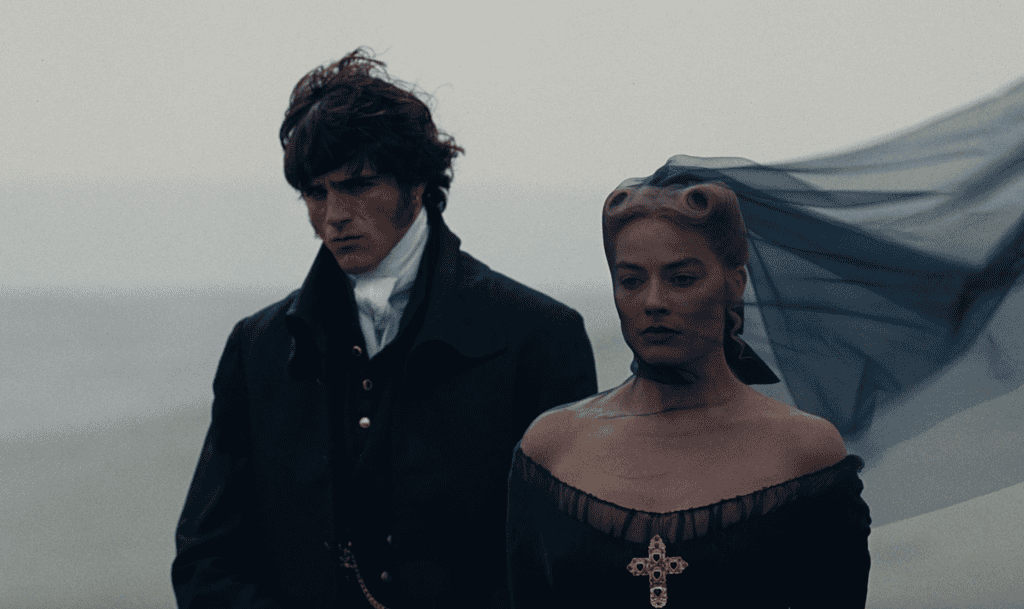 Two people in dark, old-fashioned clothing stand against a foggy, muted backdrop. The woman wears a black dress with a gold cross necklace and a sheer black veil blowing behind her. The man looks somber, gazing downward.