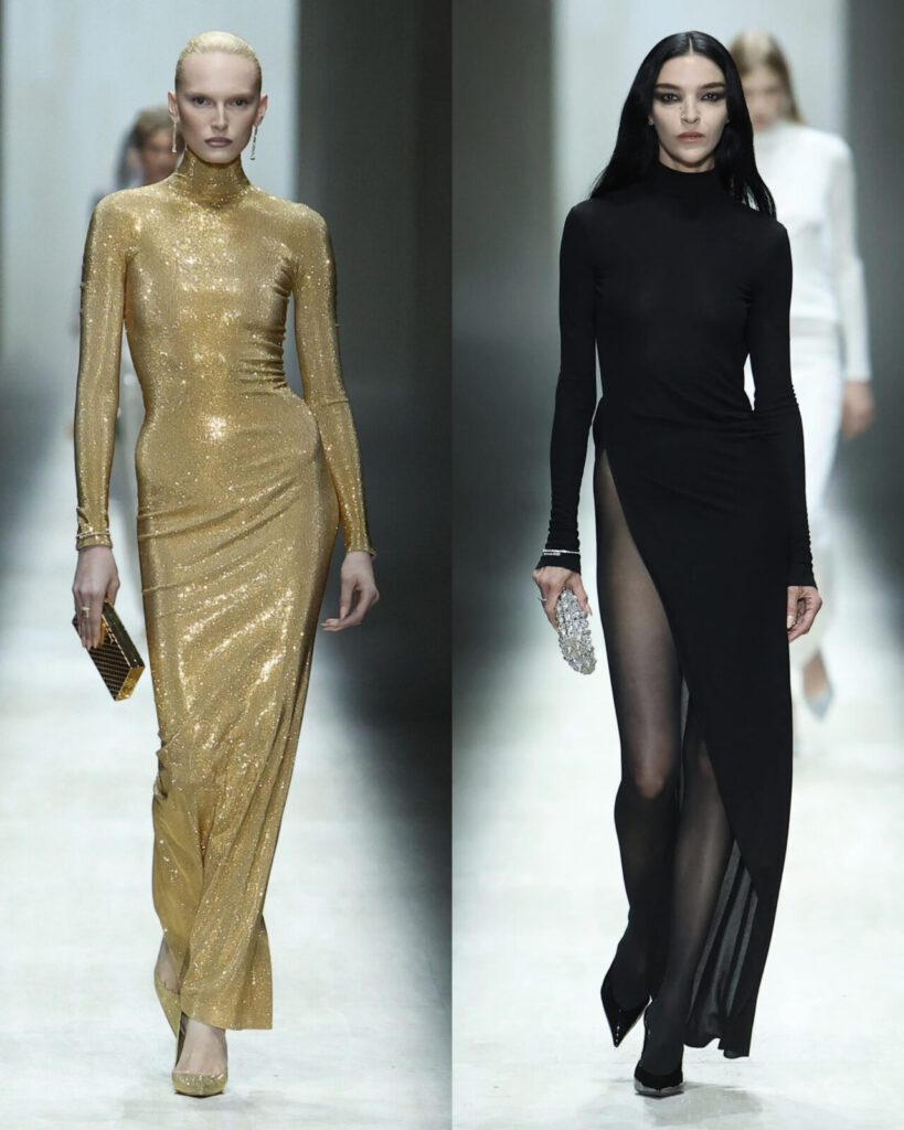 Two models walk a runway. The left model wears a shimmering gold high-neck gown and holds a matching gold clutch. The right model wears a long-sleeved black gown with a high slit and carries a silver clutch. Both have sleek hairstyles.