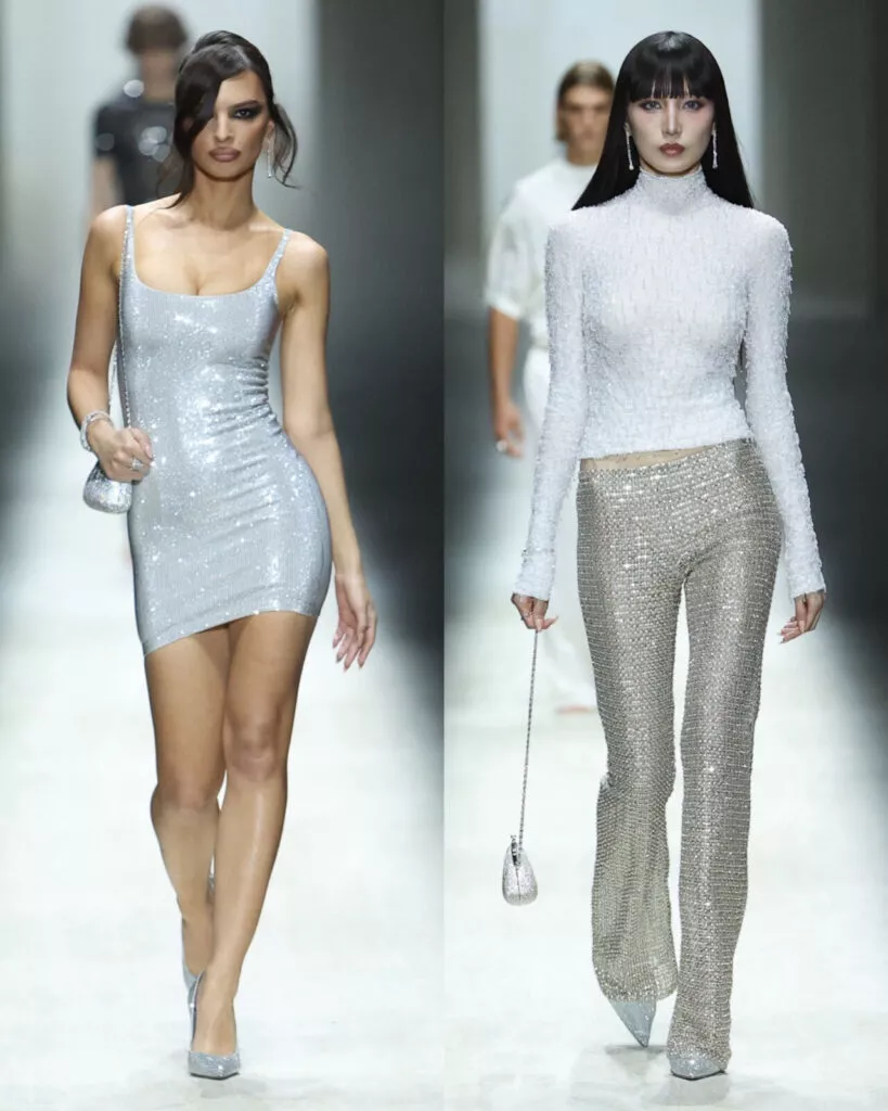 Two runway models showcase sparkly silver outfits of Gucci AW26; the left model wears a sleeveless mini dress, and the right model wears a long-sleeve turtleneck top with matching pants. Both carry small silver bags and wear silver heels.
