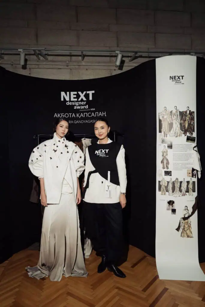 Kazakhstani designer Akbota Kapsalan posing with her model at Visa Fashion Week, showcasing the "Qara Qandyagash" collection which earned her 3rd place in the NEXT Designer Award.