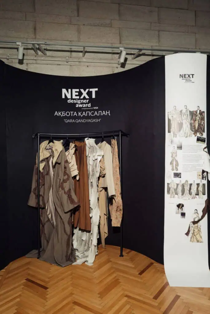 he exhibition booth for Akbota Kapsalan’s "Qara Qandyagash" collection at Visa Fashion Week Tashkent, featuring earth-toned garments and design sketches.