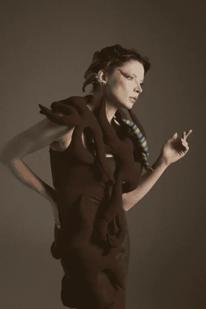 An editorial profile shot of a model wearing a dark No.sugar garment adorned with intertwined fabric "roots," highlighting the brand's focus on organic shapes and Uzbek heritage.