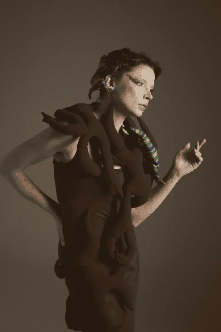 An editorial profile shot of a model wearing a dark No.sugar garment adorned with intertwined fabric "roots," highlighting the brand's focus on organic shapes and Uzbek heritage.