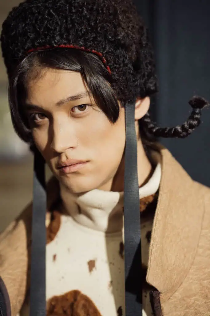 Close-up portrait of a model wearing a traditional-inspired curly black wool hat and a high-neck sweater with brown faux fur accents from Akbota Kasymbek’s VFWA collection.