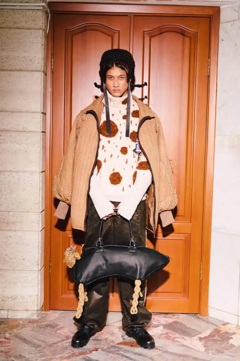 A full-length shot of a "Kökpar" collection look, including a quilted tan jacket, faux fur spotted sweater, and a black leather bag with rope legs at Visa Fashion Week Almaty.
