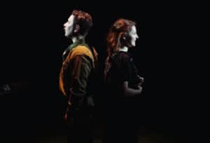 Lead actors Preston Nyman and Eva Feiler standing back-to-back in period costumes, symbolizing the long-distance connection in Dear Jack, Dear Louise.