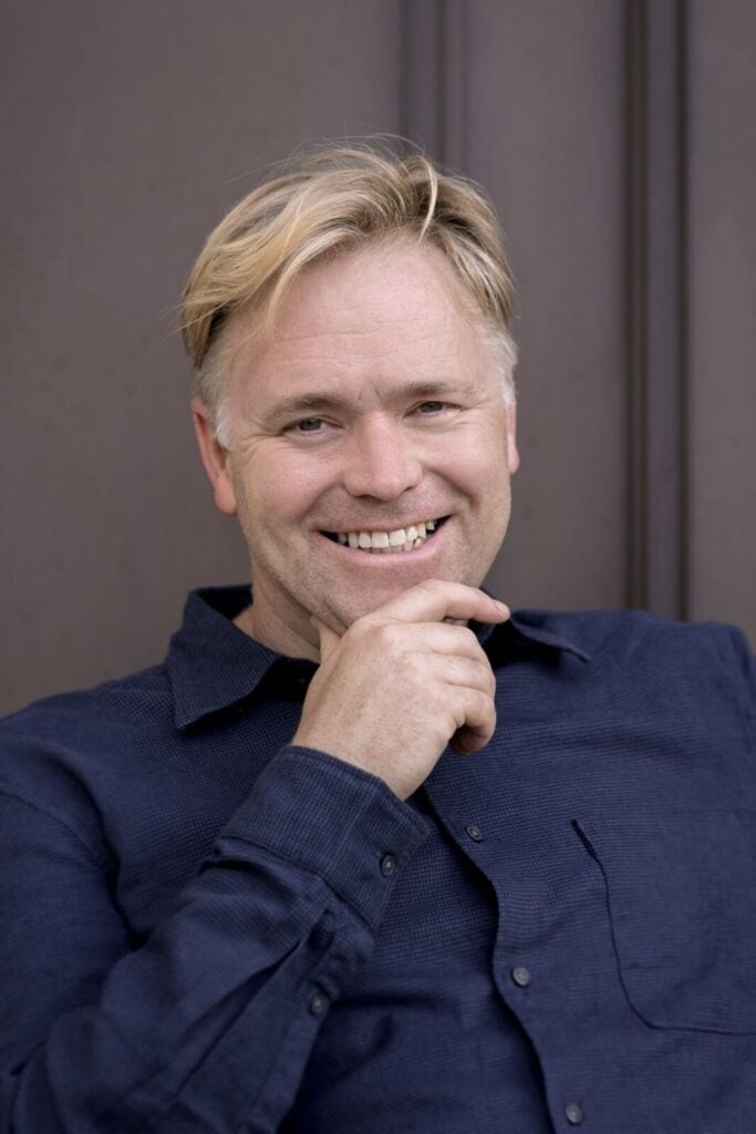 A close-up portrait of Graeme Richardson, The Times’ poetry critic and author, smiling while wearing a dark blue shirt against a neutral background.