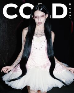 Dark pop artist DeathbyRomy on the digital cover of The Cold Magazine, wearing a pink and white tutu-style dress with long black hair, set against a dark background.