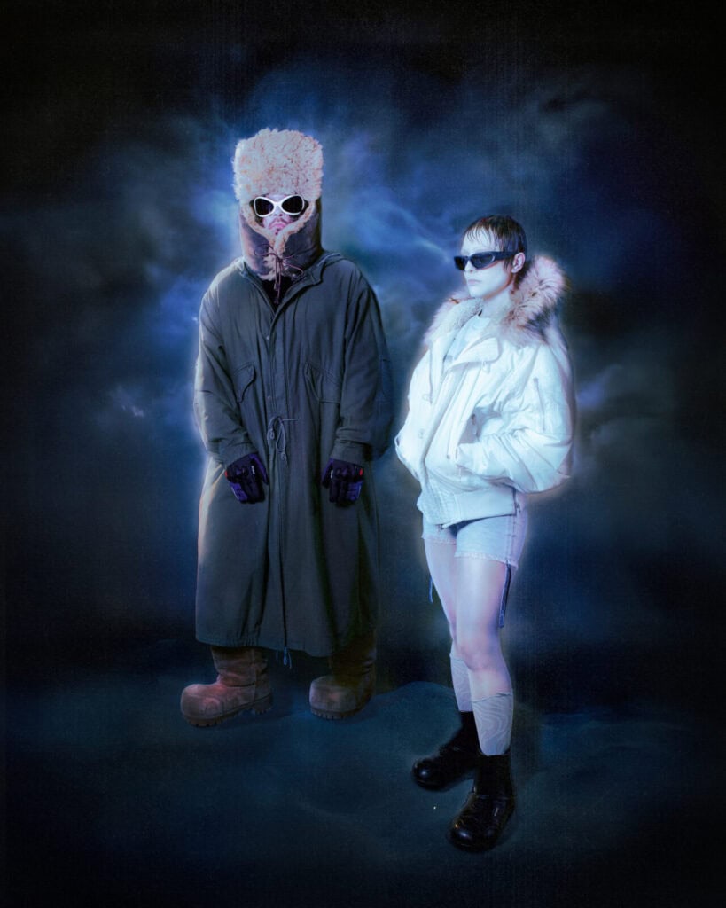 A stylized promotional photo of Pearly Drops members Sandra Tervonen and Juuso Malin wearing oversized winter gear and sunglasses against a dream-like blue background.