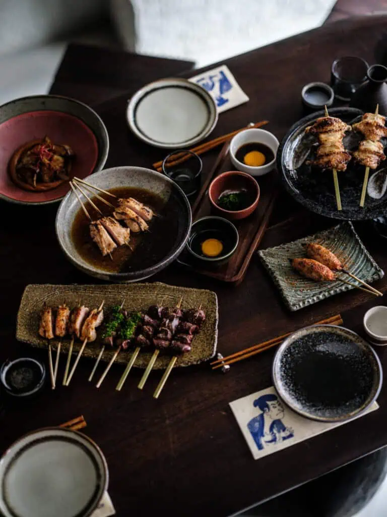 A variety of Japanese yakitori skewers, including chicken cuts and dipping sauces with egg yolk, served on artisanal plates at Yuzu Dining Bar, Amsterdam.