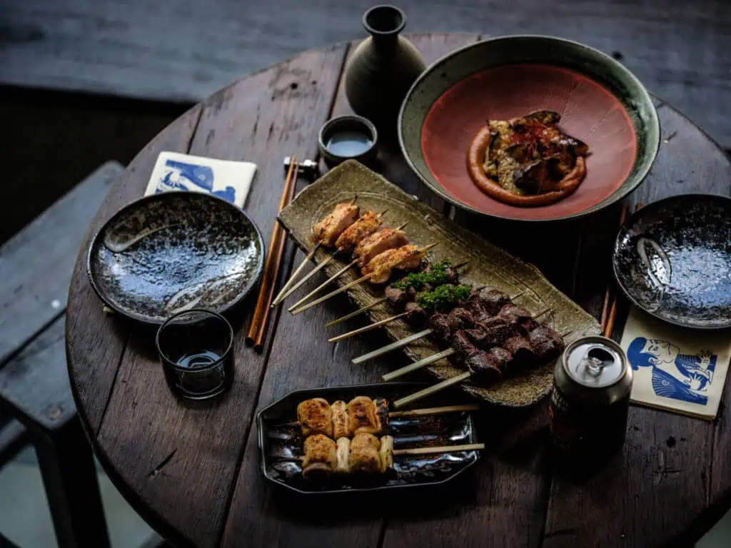 Traditional coal-fired Japanese yakitori and small plates served on a rustic wooden table, showcasing the classy dining experience at Amsterdam's Yuzu Dining Bar.