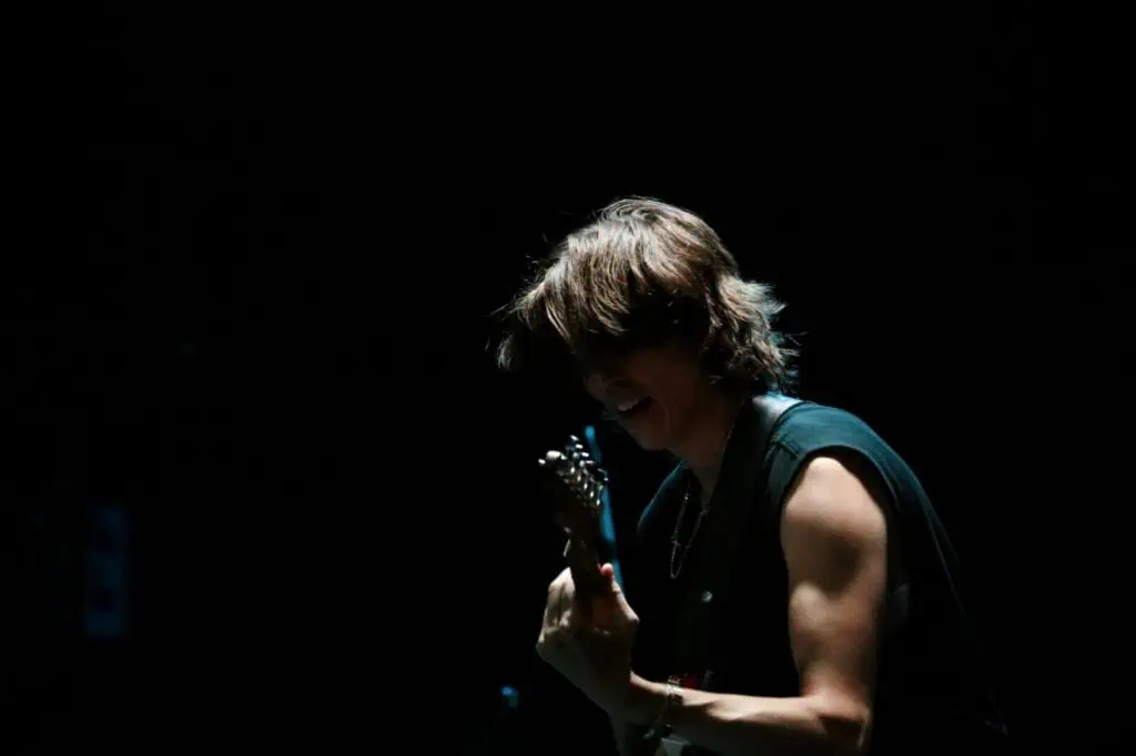 Side profile of E.R. Fightmaster playing electric guitar on a dark stage under a spotlight