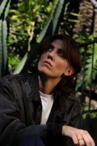 E.R. Fightmaster in a denim jacket looking up, with green cactus plants in the background