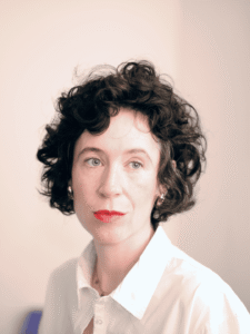 Close-up portrait of Niamh Campbell with dark curly hair and a white shirt
